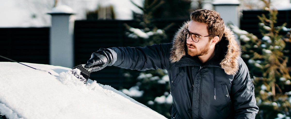 Mann entfernt Eis und Schnee mit einem Lyvanas Eiskratzer vom Auto
